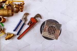 Shower drain surrounded by various plumbing parts and tools