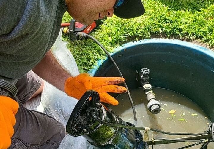 Expert Plumber Servicing a Grinder Pump-169-28zo17 Plumber kneeling by a lift station reservoir, working on a grinder pump