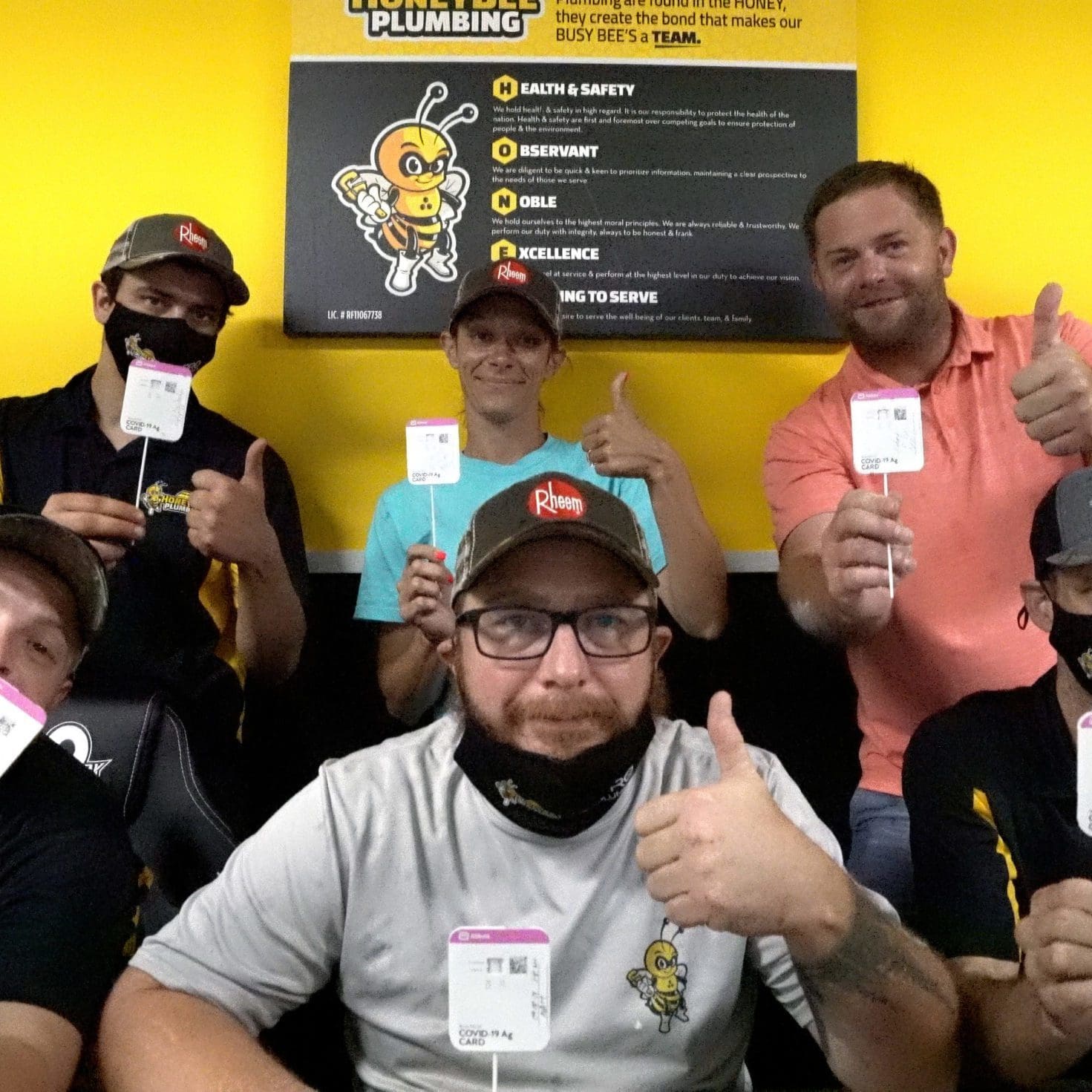 Honey Bee Plumbing team standing in front of a core values poster, celebrating their negative COVID-19 test results